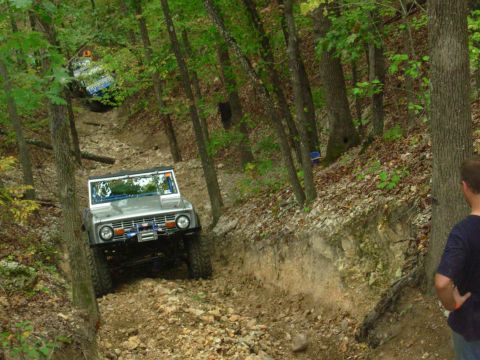 1983 Ford Bronco - A silver 1978 Ford Bronco navigates a steep, wooded off-road trail, with another vehicle visible further up the path.