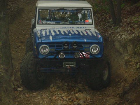 1983 Ford Bronco - This modified off-road vehicle, likely a 1973 Ford Bronco, navigates a dirt trail with oversized tires and auxiliary lights.