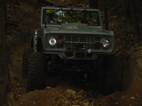1983 Ford Bronco - Ford Bronco navigating a rough, wooded trail with significant suspension articulation.