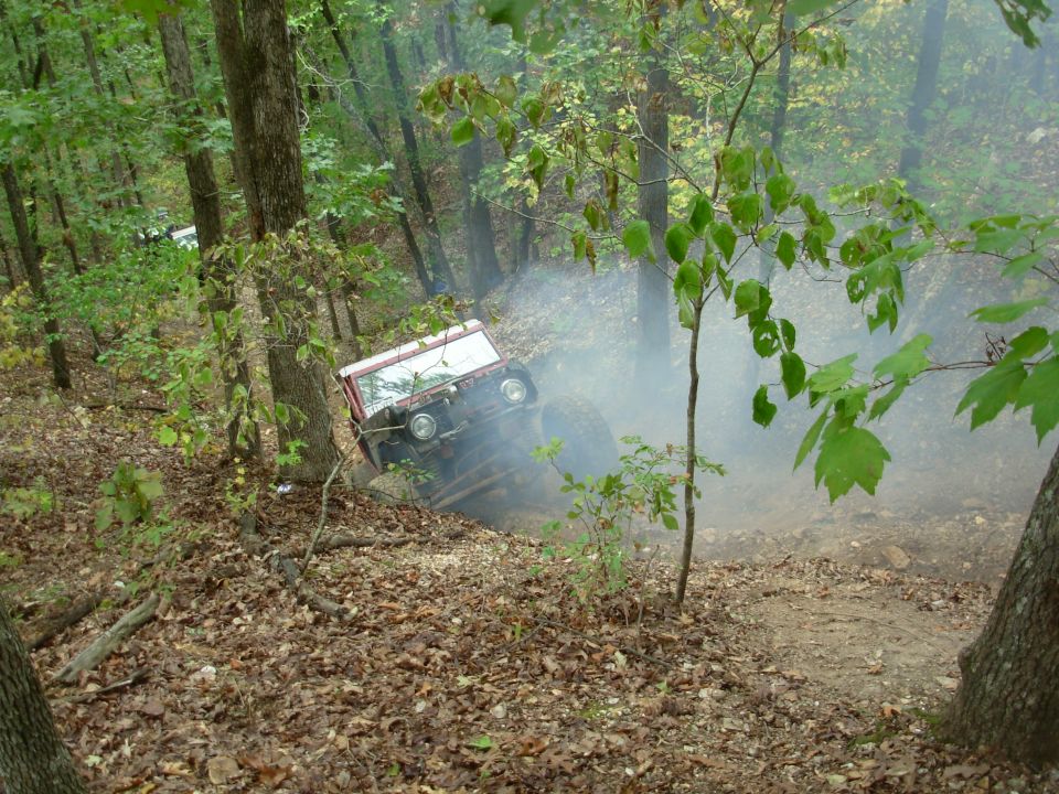White and red topless 4x4 leaning off-camber on a leafy wooded slope in drifting dust