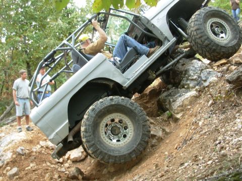 1983 Ford Bronco - An off-road vehicle navigates a steep, rocky terrain with two spectators watching.