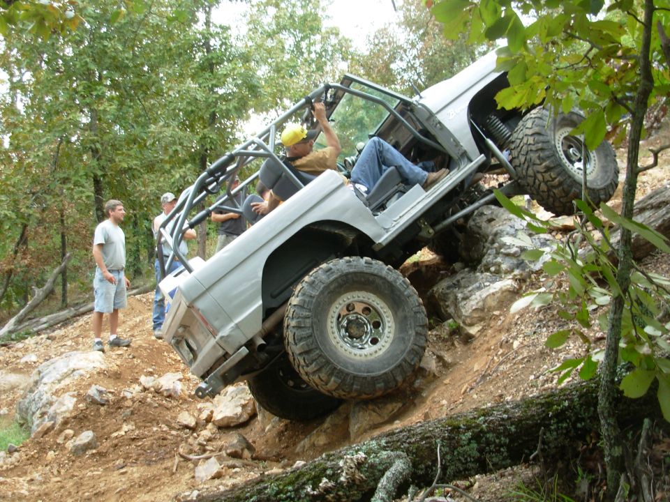 White caged doorless Bronco trail rig climbing rock ledge with rear wheel lifted