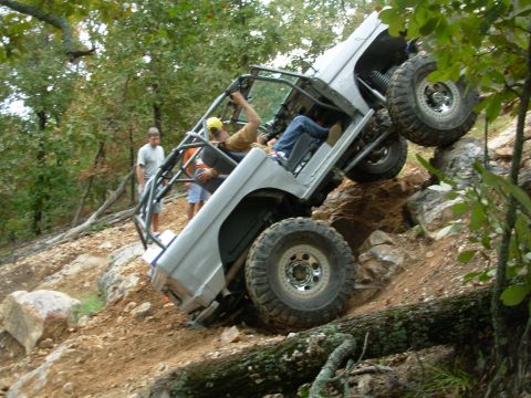 1983 Ford Bronco - A heavily modified off-road vehicle navigates a steep, rocky trail with two people inside and another person watching.