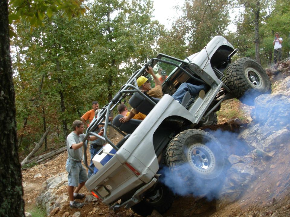 White caged rock crawler climbing a steep rock ledge nose-high with tire smoke