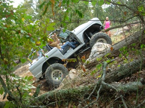 1983 Ford Bronco - An off-road vehicle navigates a challenging, wooded terrain with a steep incline and fallen logs.