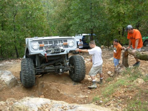 1983 Ford Bronco - An off-road SUV with large tires navigates a dirt incline, with several people observing the action.