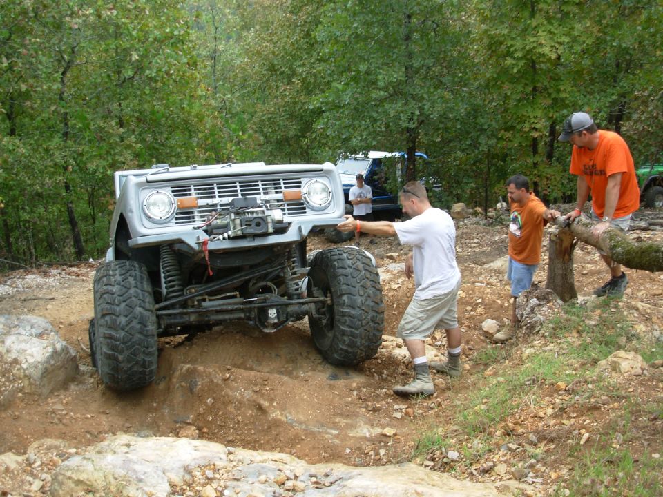 Silver early Ford Bronco with winch and mud tires flexing over rocks on a trail