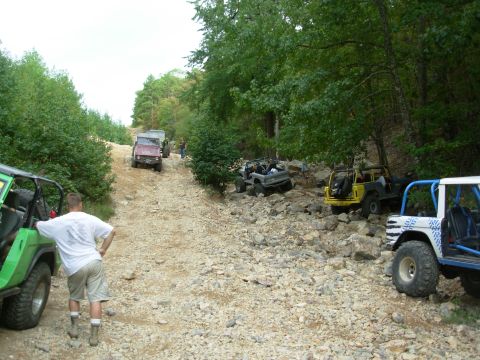 1983 Ford Bronco - Several off-road vehicles navigate a challenging rocky trail, including a white 1983 Ford Bronco in the foreground.