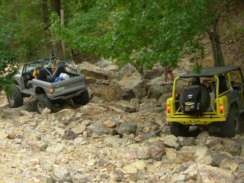 1983 Ford Bronco - Two Broncos tackle a challenging rocky trail in a wooded area.