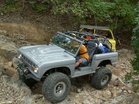 1983 Ford Bronco - Two off-road vehicles navigate a rocky trail, with the lead Bronco modified for extreme terrain.