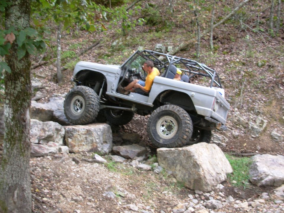 White early Ford Bronco with roll cage crawling over limestone boulders in wooded rock garden