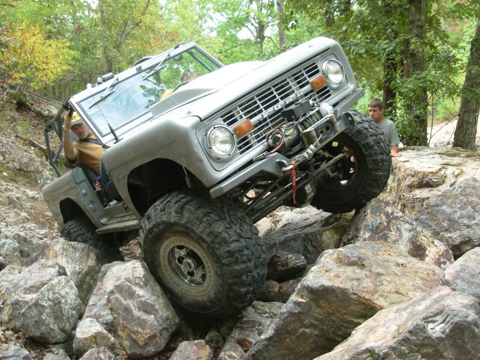 Silver doorless early Bronco with winch climbing boulders, tipped onto one front tire