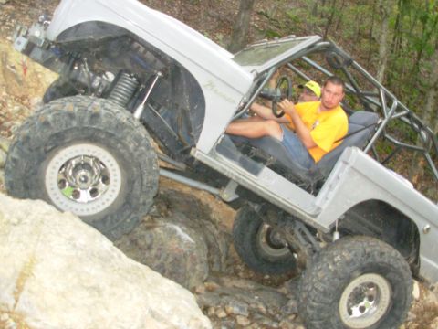 1983 Ford Bronco - This modified off-road vehicle navigates a rocky terrain with its occupants.