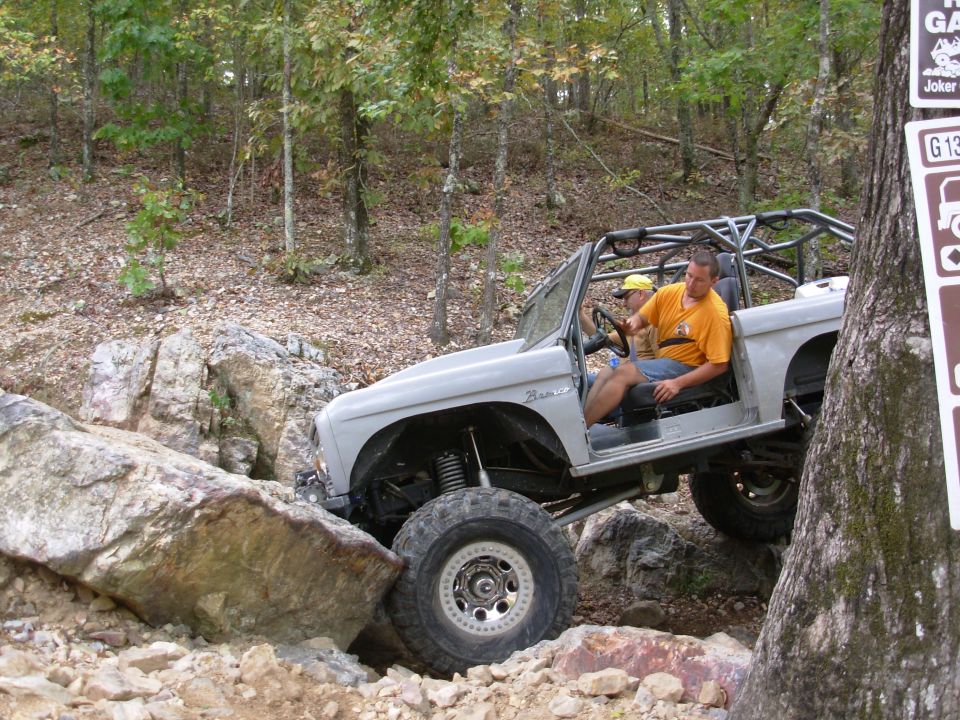 White caged Ford Bronco rock crawling over boulders with driver at the wheel