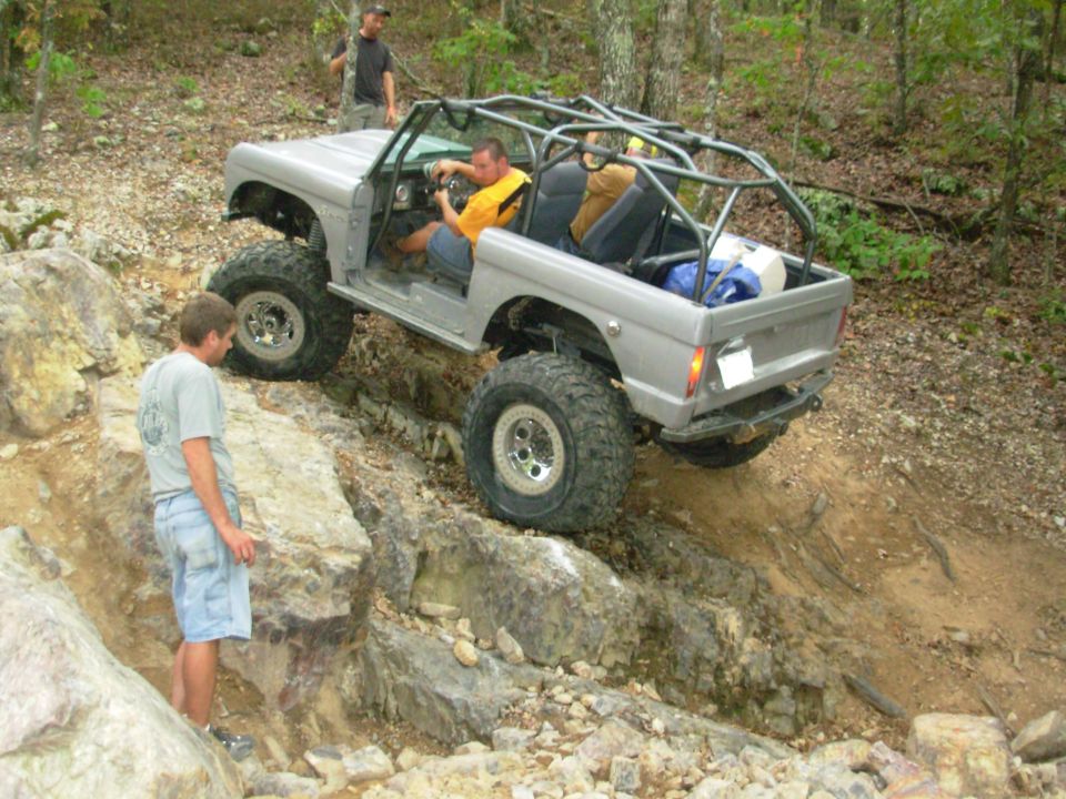 Silver caged doorless Ford Bronco crawling a rock garden with driver and spotters