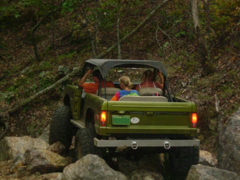 1983 Ford Bronco - This SUV is navigating a rocky trail in a wooded area with several passengers.