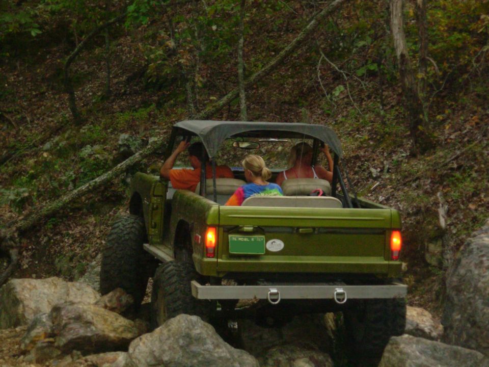 Green early Ford Bronco with bikini top crawling over boulders, rear view