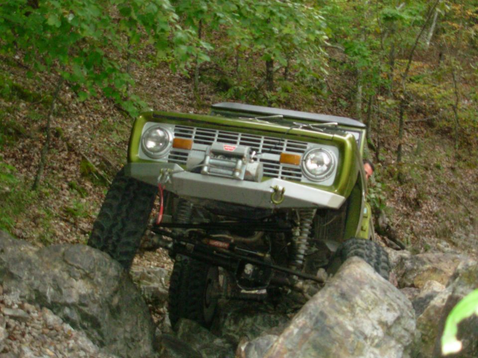 Green early Ford Bronco with Warn winch climbing rocks, front suspension exposed