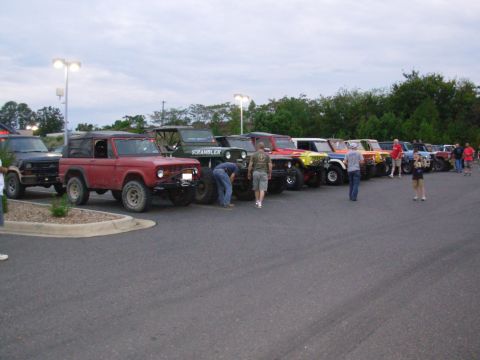 1983 Ford Bronco - A line of SUVs, including a red Ford Bronco, are parked in a lot under an overcast sky.