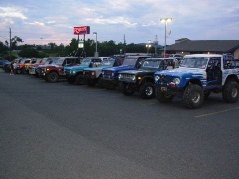 1983 Ford Bronco - Several Ford Broncos are parked in a lot, some with modifications, under a cloudy sky.