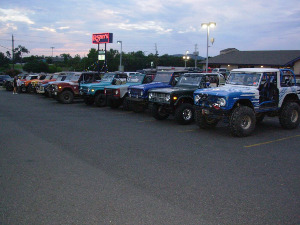 Row of lifted early Ford Broncos parked at dusk outside a Ryan's restaurant