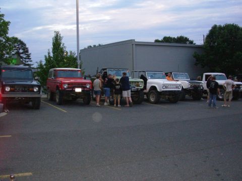1983 Ford Bronco - A group of Ford Broncos are gathered in a parking lot under a cloudy sky.