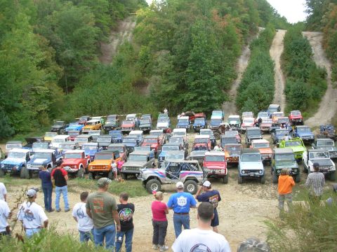 1983 Ford Bronco - A large collection of Ford Broncos gathered for an off-road event, with many vehicles parked on a dirt lot and hills in the background.
