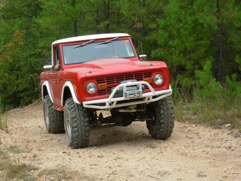 1983 Ford Bronco - This red Ford Bronco, modified for off-road use, is captured from a 3/4 front angle on a dirt path.