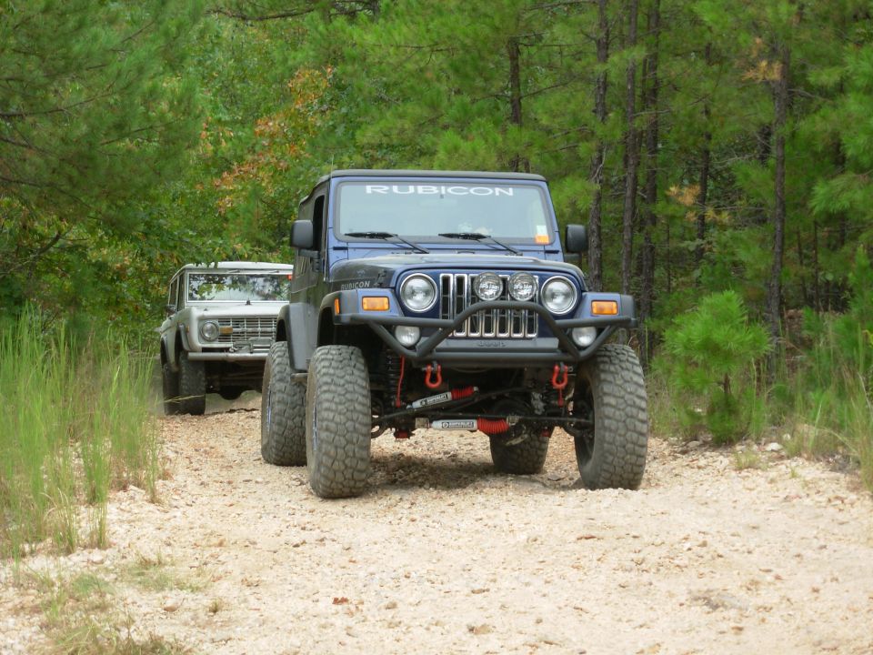 Dark blue Jeep Wrangler Rubicon on gravel trail with early Bronco behind