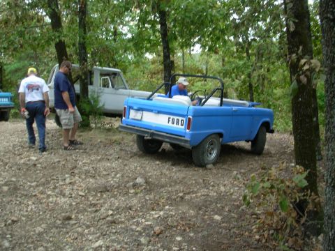 1983 Ford Bronco - A blue convertible SUV with 'FORD' on the tailgate is parked outdoors with other vehicles and people.