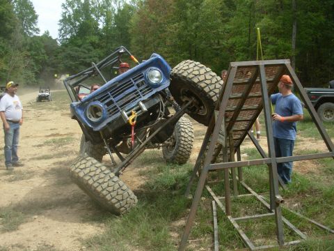 1983 Ford Bronco - A modified blue Ford Bronco navigates an off-road obstacle course, with spectators watching.