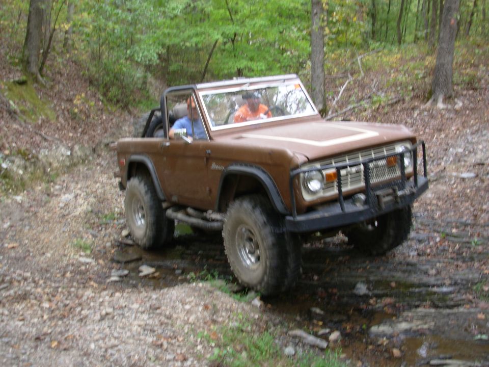 Brown topless early Bronco with brush guard and winch on rocky wooded creek trail