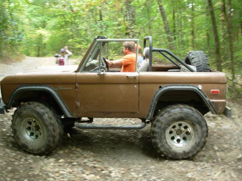 1983 Ford Bronco - A brown Ford Bronco is driven off-road through a wooded area.