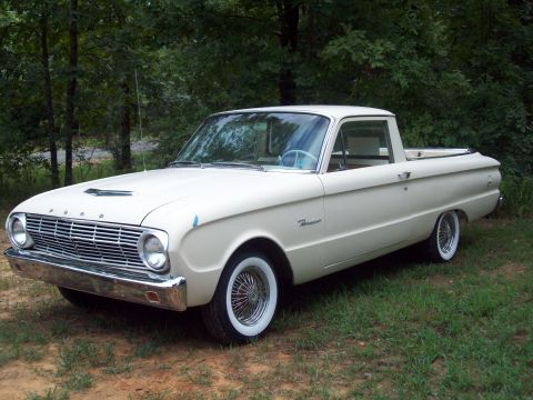 1963 Ford Ranchero - A white 1963 Ford Ranchero pickup truck is shown from a three-quarter front view, parked on a grassy area with trees in the background.