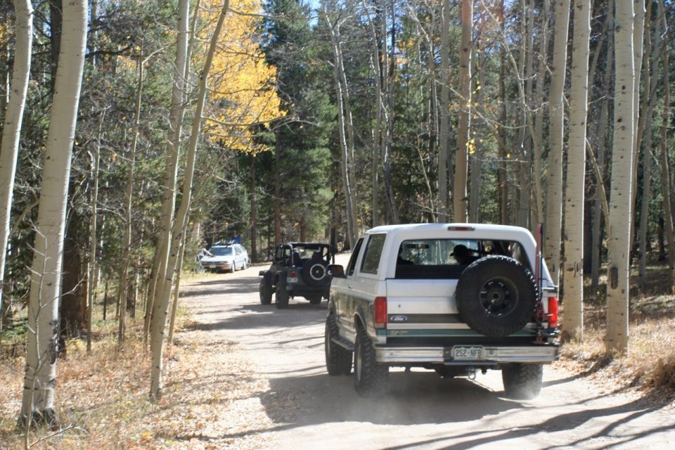 1996 Ford Bronco driving on a dirt road with two other vehicles behind it