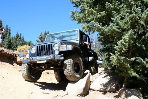 1996 Ford Bronco - A Jeep Wrangler TJ tackles a challenging rocky trail in a wooded, mountainous area.