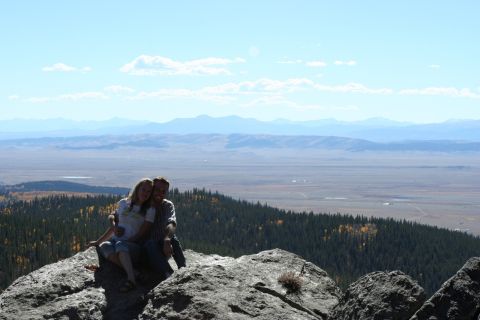 1996 Ford Bronco - A couple enjoys a scenic vista from a rocky outcrop, with distant mountains and a wide valley stretching out before them.