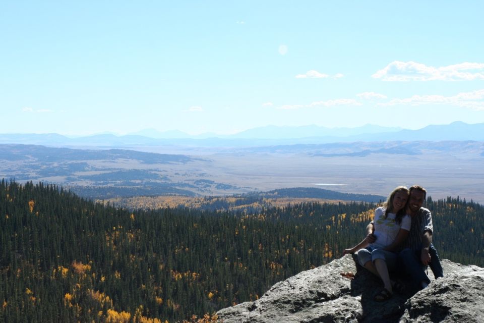 Couple sits on a rock with a vast valley and mountains in the background