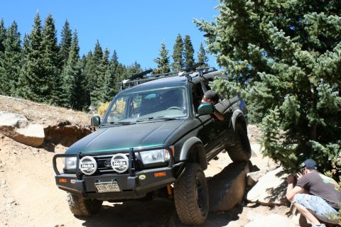 1996 Ford Bronco - SUV is shown off-roading on a dirt path with trees and rocks.