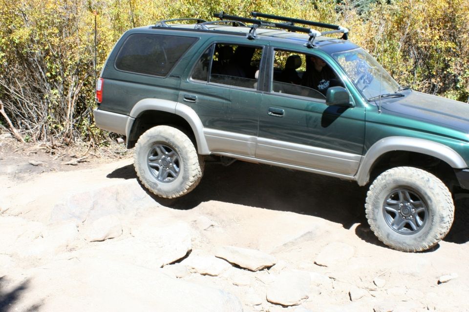 Green SUV with roof rack driving over rocks, two-tone paint, off-road tires