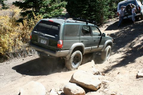 1996 Ford Bronco - A green SUV navigates a challenging rocky trail, with another vehicle visible in the background.