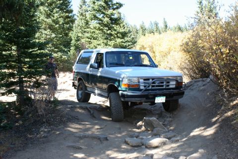 1996 Ford Bronco - This 1996 Ford Bronco navigates a challenging, rocky off-road path surrounded by trees.