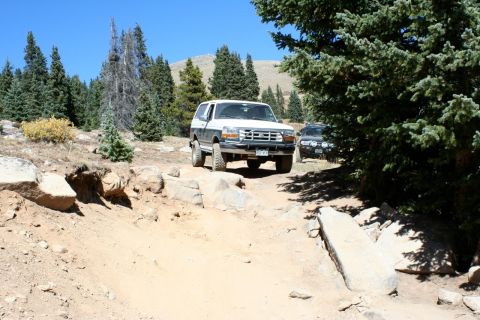 1996 Ford Bronco - 1996 Ford Bronco navigates a challenging off-road trail in a mountainous, wooded area.