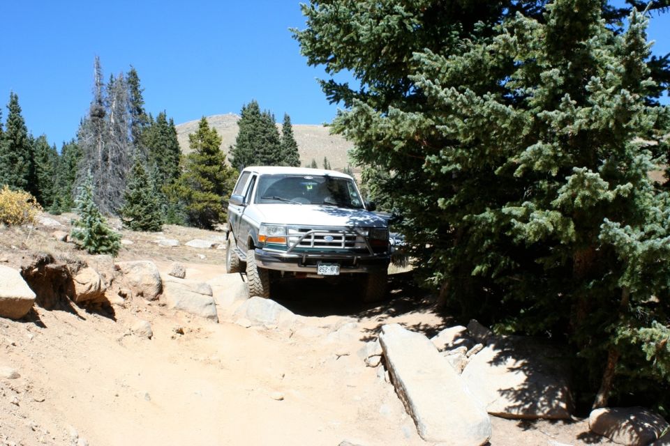 White Ford Bronco navigating a rocky trail with trees and mountains in the background