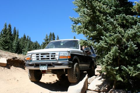 1996 Ford Bronco - 1996 Ford Bronco navigates a challenging off-road path through a wooded area.