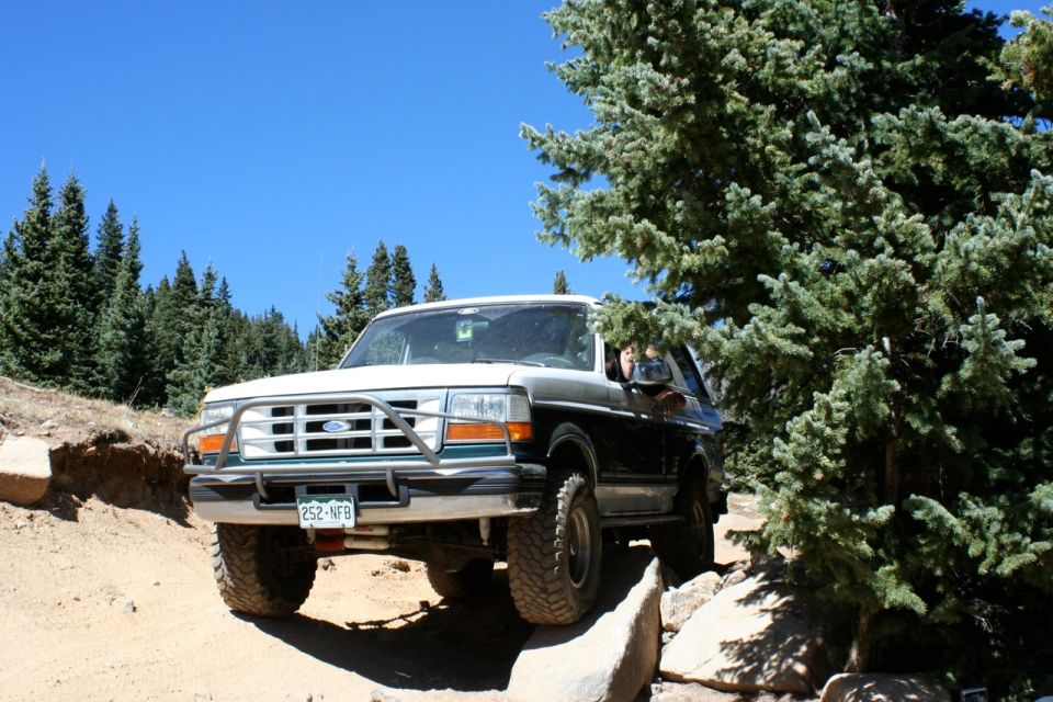 1996 Ford Bronco driving on a rocky, dirt trail with trees on the right