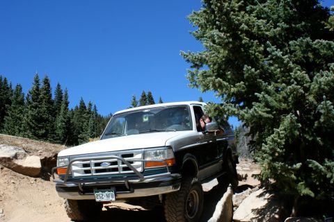 1996 Ford Bronco - A 1996 Ford Bronco navigates a rocky off-road trail under a clear blue sky.