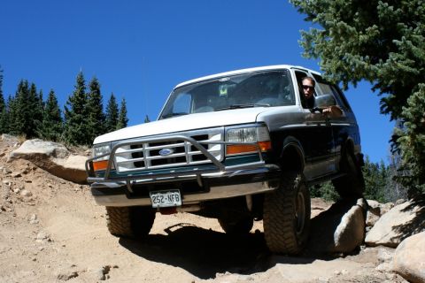 1996 Ford Bronco - A 1996 Ford Bronco navigates a challenging rocky terrain under a clear blue sky.