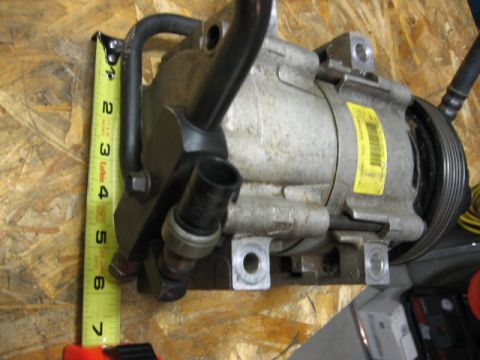 1995 Ford Bronco - A close-up of an air conditioning compressor, with a tape measure indicating its size.