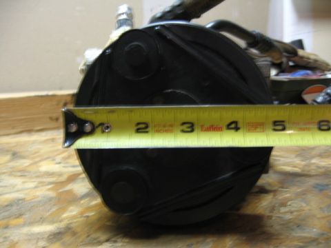 1995 Ford Bronco - A yellow tape measure is used to measure the diameter of a black automotive AC compressor.
